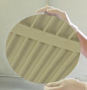 Ø300mm glass plate with mirror like Nb deposit realized by multi beam sputtering Photo of gloved hands holding a Ø300mm glass plate with a mirror like deposit reflecting the ceiling, realized by multi beam sputtering