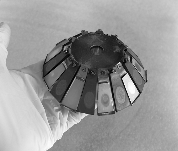 Example of a target block for multi beam sputter deposition on circular substrates, with 10 targets of material A, alternating with 10 targets of material B Photo of gloved hand holding a conical target block typical for multi beam sputter deposition on circular substrates, with 10 targets of material A, alternating with 10 targets of material B