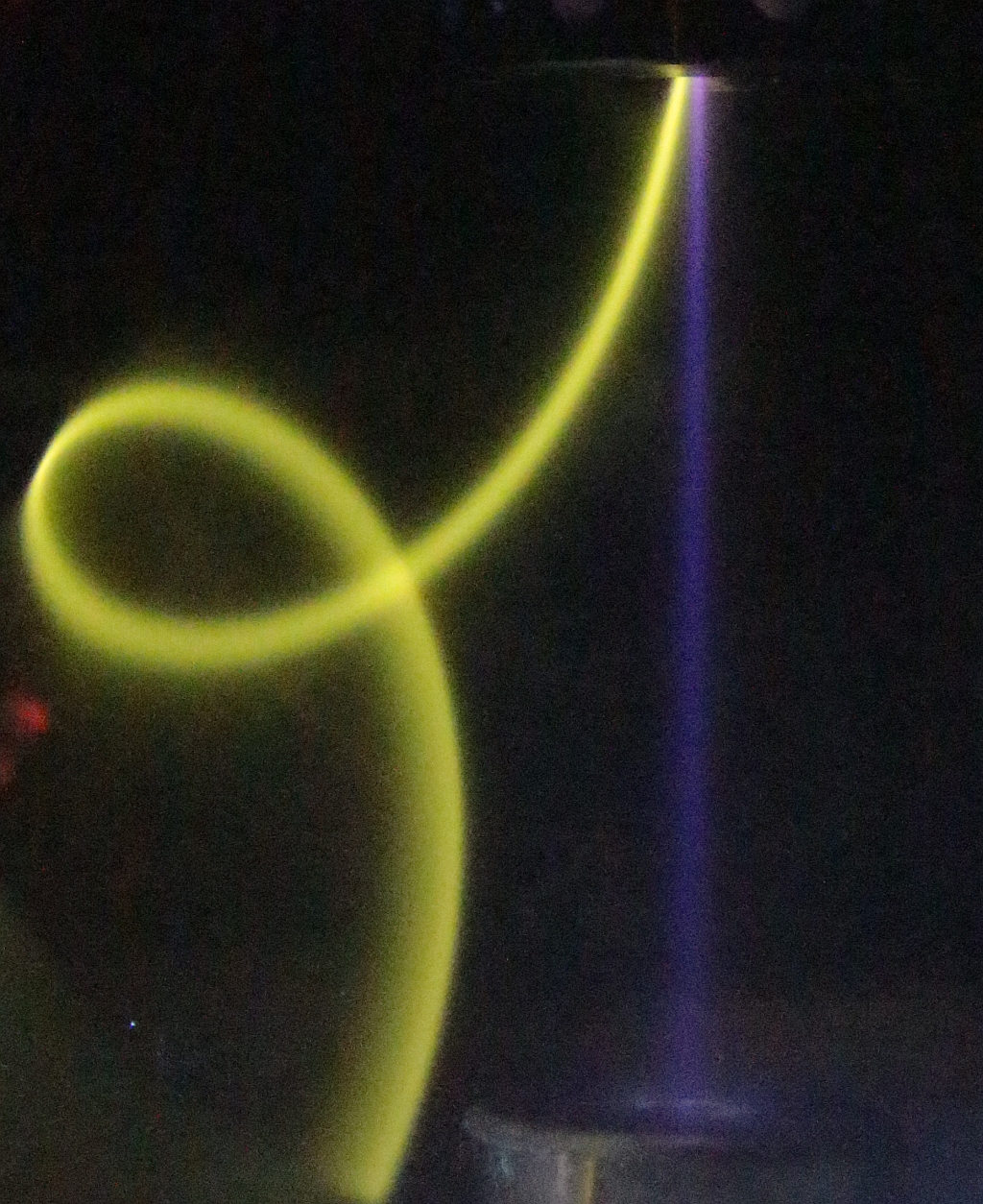 TES as negative ion source : blue parallel beam of negative oxygen ions, and curly yellow beam of magnetically deflected electrons Photo of the TES ion source facing a Faraday cup, showing a blue parallel beam of negative oxygen ions, and a curly yellow beam of magnetically deflected electrons
